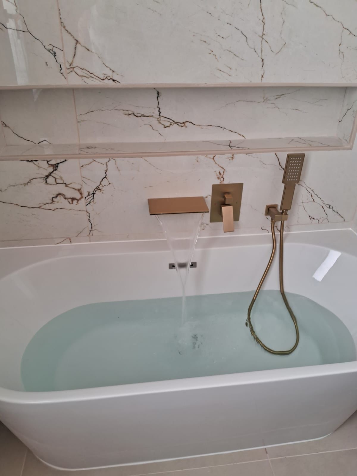 Salle de bain après travaux : baignoire îlot et faïence effet marbre, robinetterie dorée